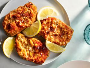 Baked breaded pork chops on a plate with lemon wedges 