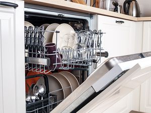 A dishwasher slightly ajar, filled with plates, bowls, cups, and silverware