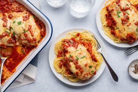Chicken parmesan over pasta on a plate served from a casserole dish nearby
