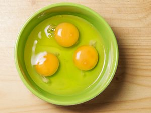 A top-down image of a green bowl filled with three raw eggs.