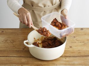person scooping beef stew into a tupperware containers