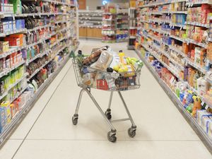 A packed grocery cart in an empty grocery aisle 