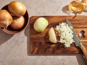 peeled onion on a cutting board partly diced, with chef's knife