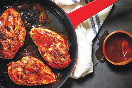 Three chicken breasts coated with barbecue sauce in a red skillet