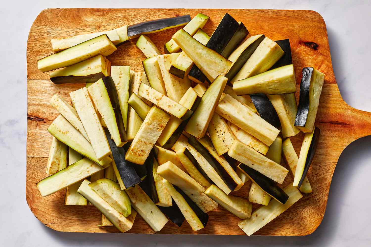 Eggplants cut into even strips on a wooden cutting board 