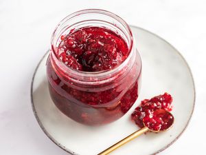 Red currant jam in a glass jar and on a spoon, set on a plate