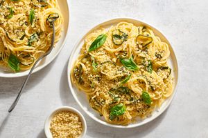 Two plates of caramelized zucchini pasta, topped with breadcrumbs and whole basil leaves
