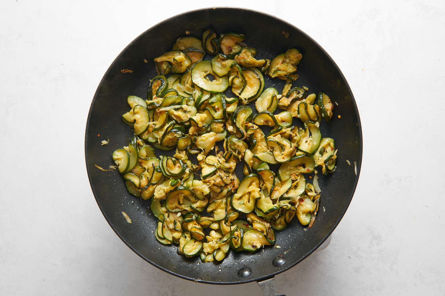 A skillet of cooked zucchini and shallots, with minced garlic and red pepper flakes