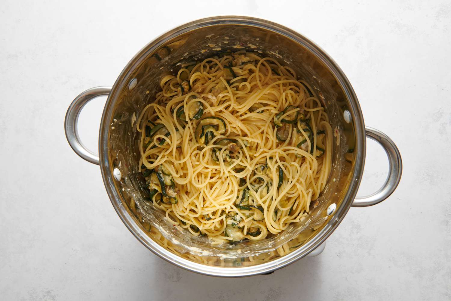 A pot of spaghetti in a cream cheese-pasta water sauce, with the zucchini-shallot mixture, topped with parmesan cheese