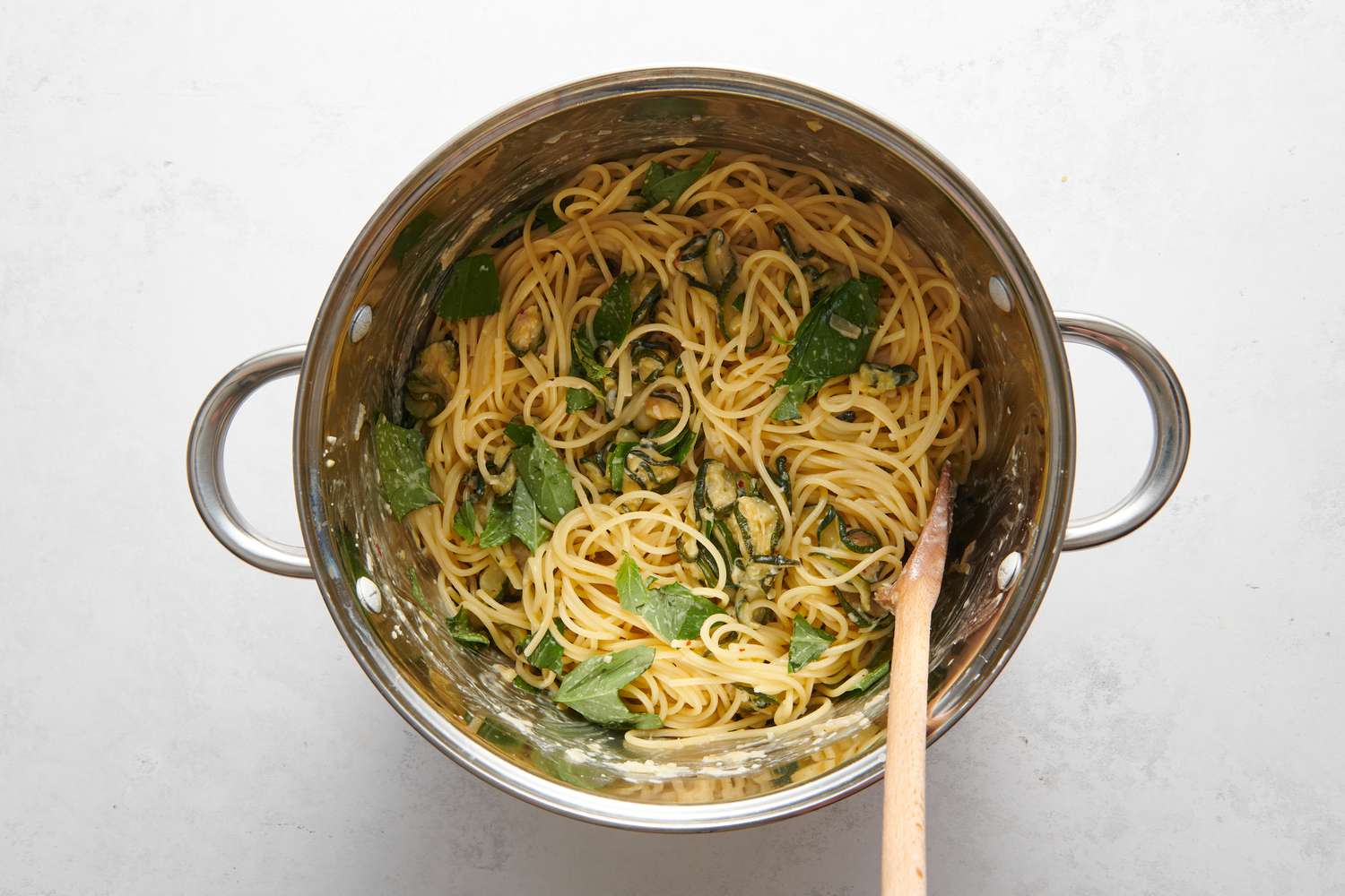 A pot of caramelized zucchini pasta topped with lemon juice and fresh basil leaves