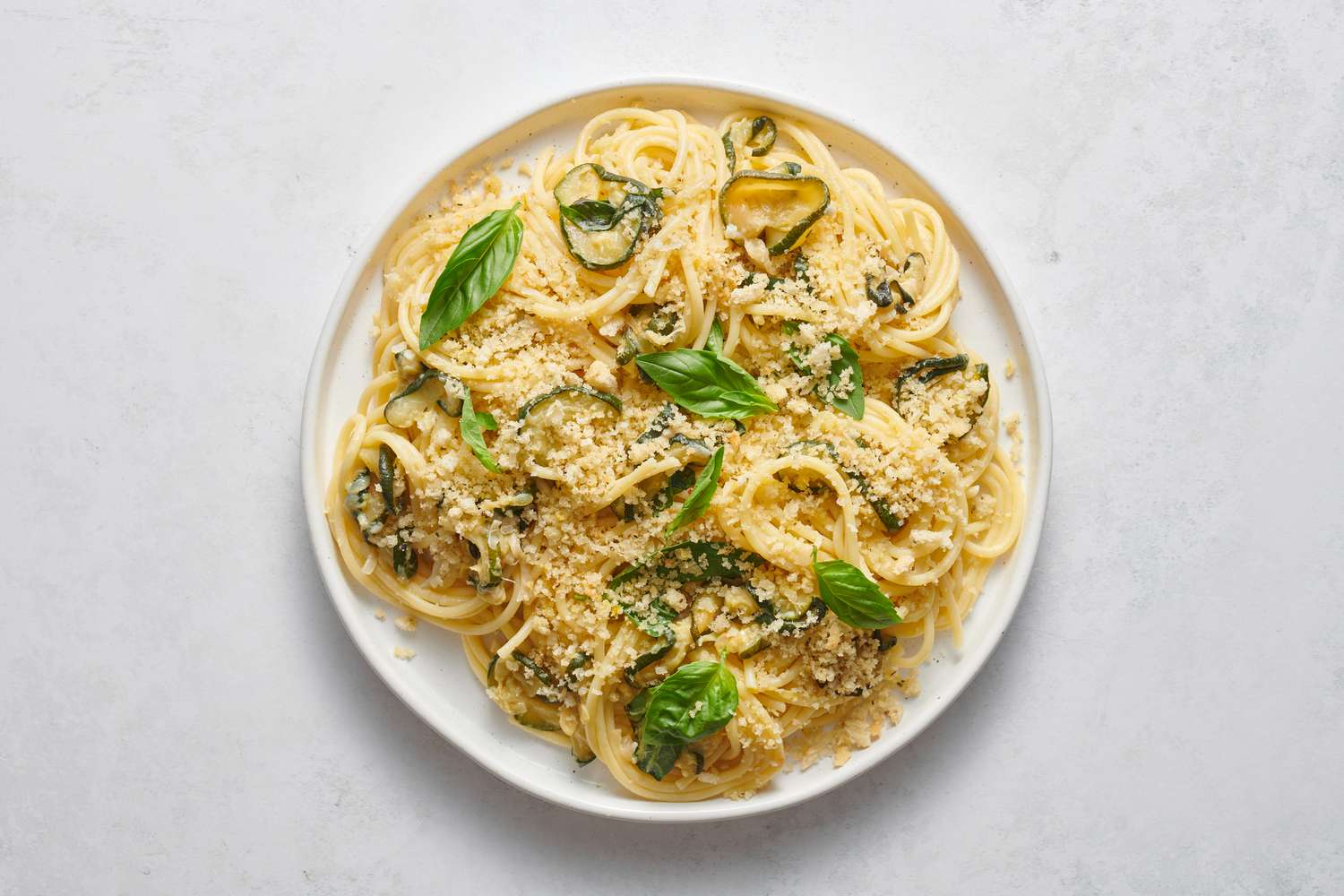 A large plate of caramelized zucchini pasta, topped with seasoned breadcrumbs and whole leaf basil