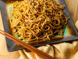 Chinese pork lo mein noodles with chopsticks on top of a gold napkin and a wooden surface