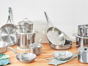 An assortment of stainless steel cookware pots and pans on a wooden kitchen counter.