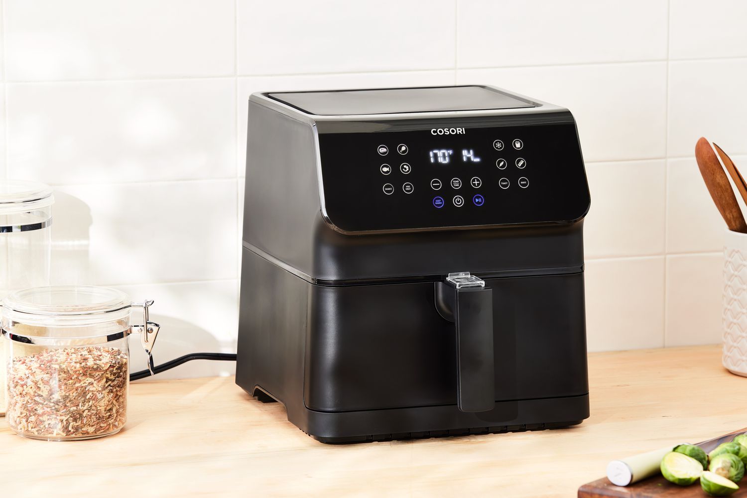 Cosori VeSync Pro II Smart Air Fryer displayed on a wood surface in front of white tile