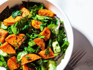 Salad in white ceramic bowl with sweet potato, onions, and greens on a marble surface