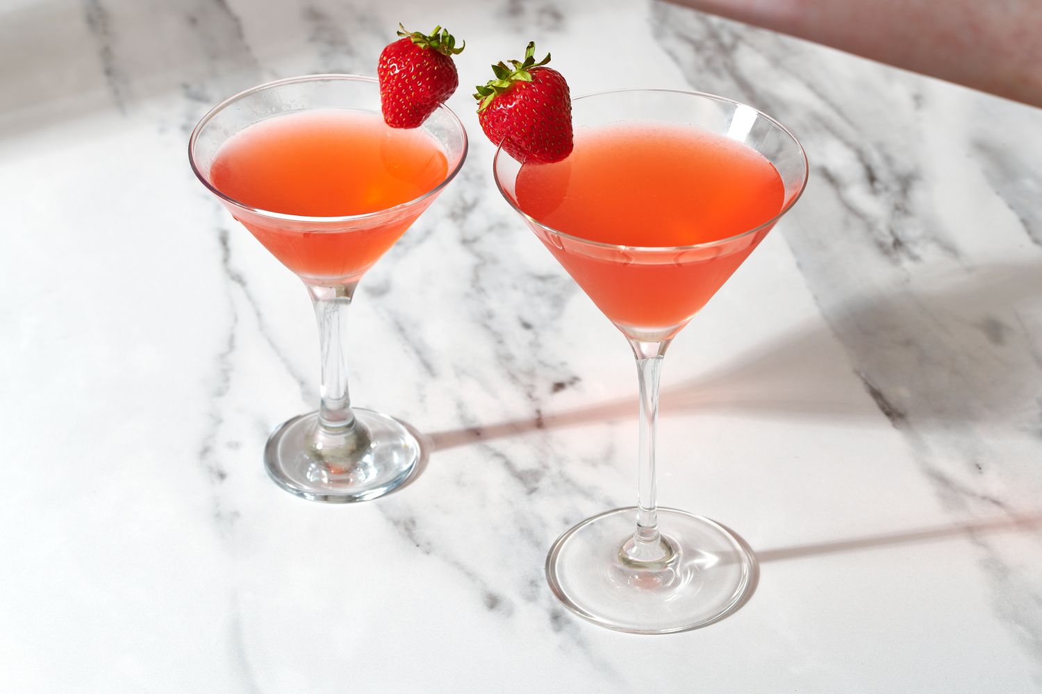 Two strawberry martinis on a marble surface, garnished with a fresh strawberry