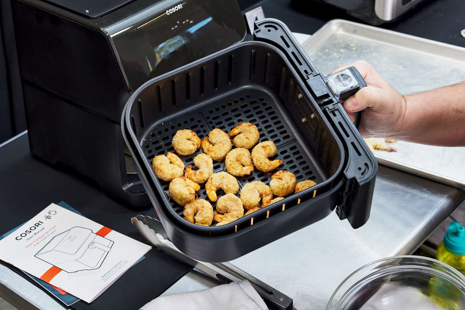 A hand holding the basket from the Cosori VeSync Pro II Smart Air Fryer full of shrimp