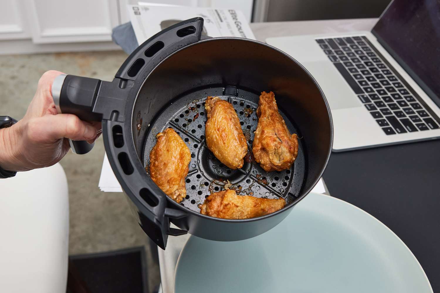 Hand holding the Dash Compact Air Fryer basket full of chicken wings