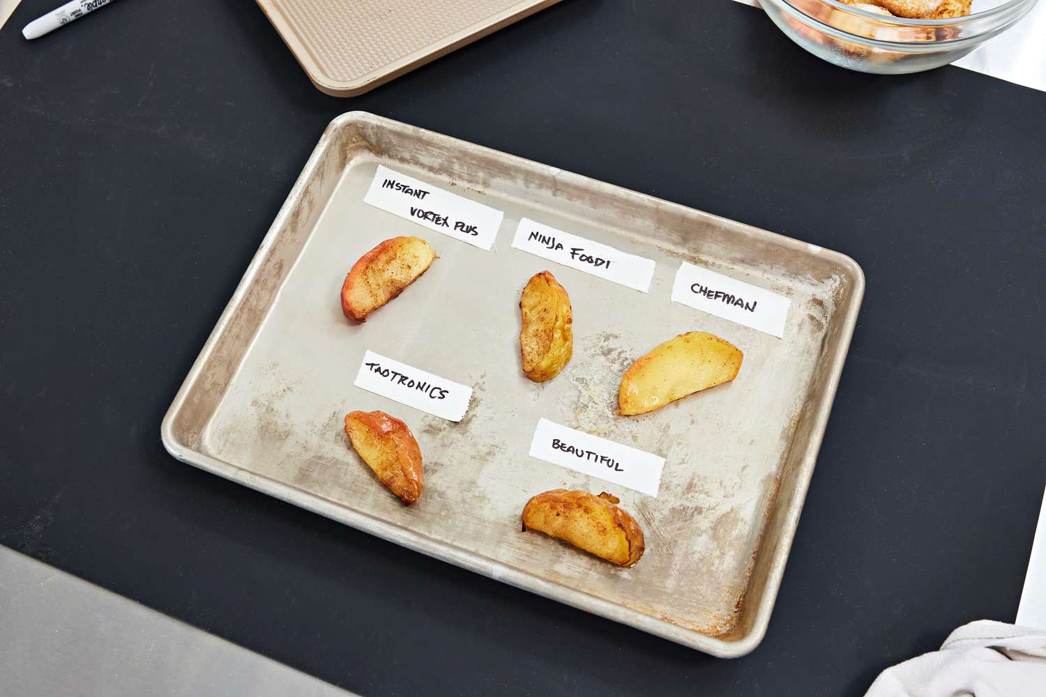 A baking sheet with pieces of food with labels of various air fryers