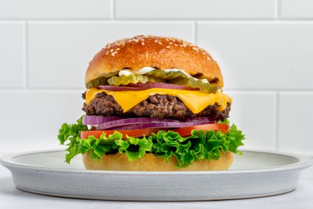 Beef burger with lettuce, tomato, onion, cheese, pickles, and mayo on a sesame bun