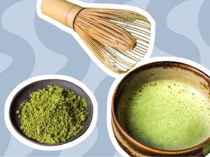 Bowl of matcha powder, cup of matcha tea, and a whisk on a blue background
