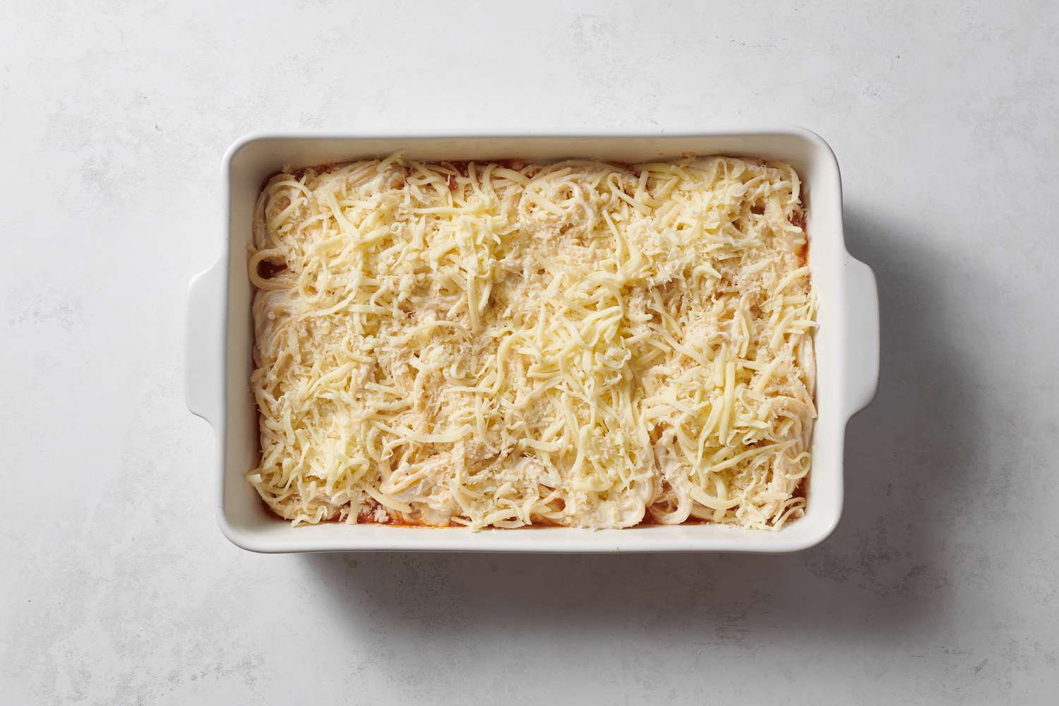 A baking dish with a layer of meat sauce, pasta mixture, and cheese