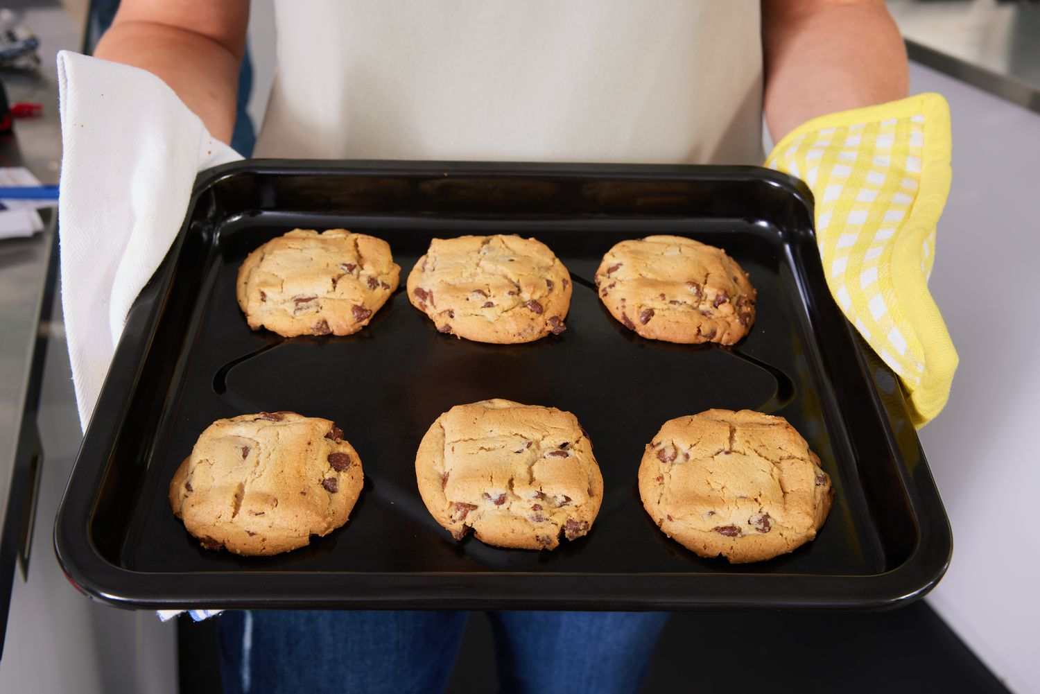 A person holding a tray of baked chocolate chip cookies 