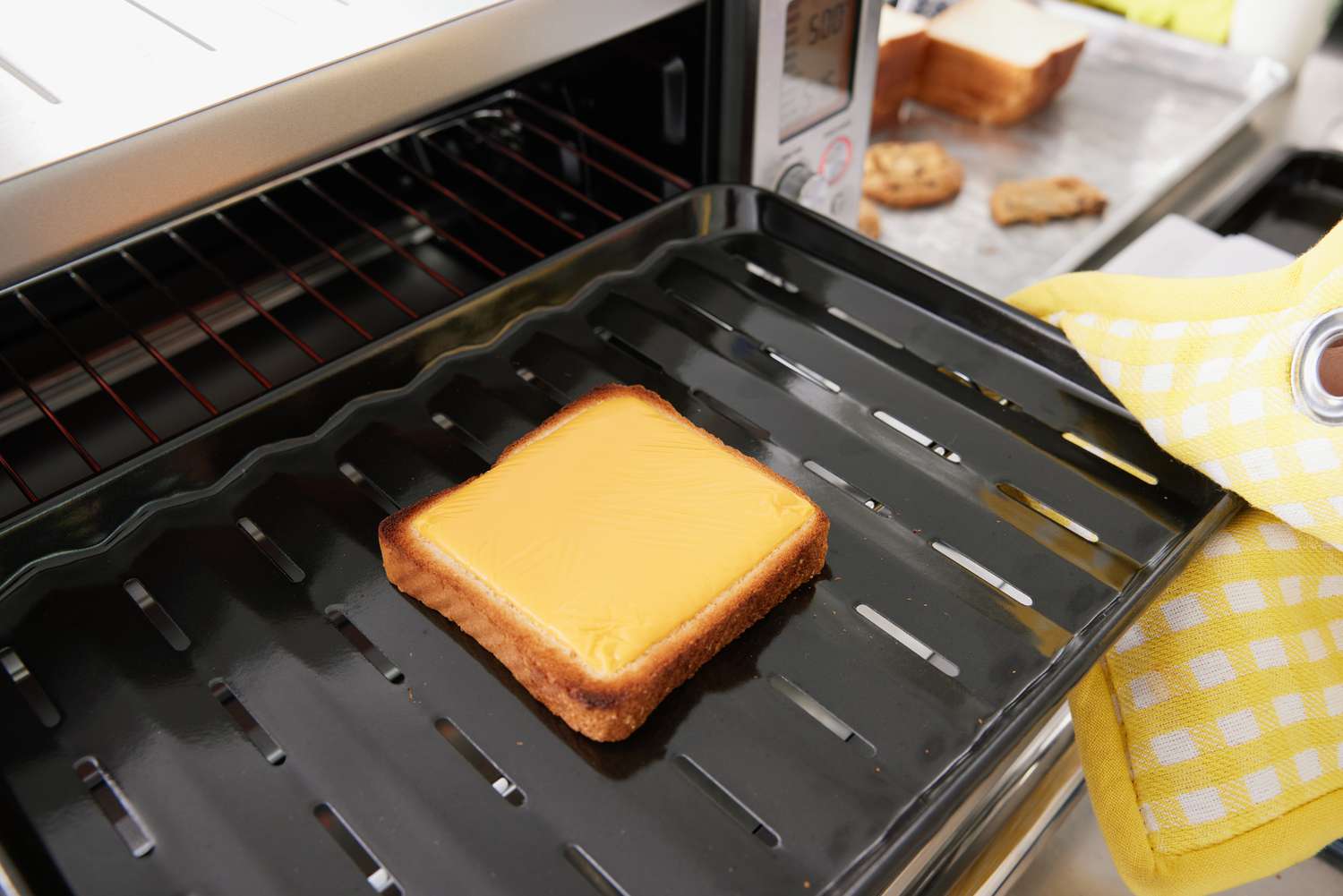 A hand with oven mitt pulling out a tray with a piece of cheese toast from the Breville Smart Oven Air Fryer