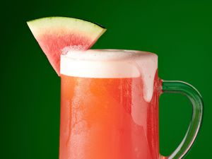 watermelon beer in pint glass with watermelon garnish on green background