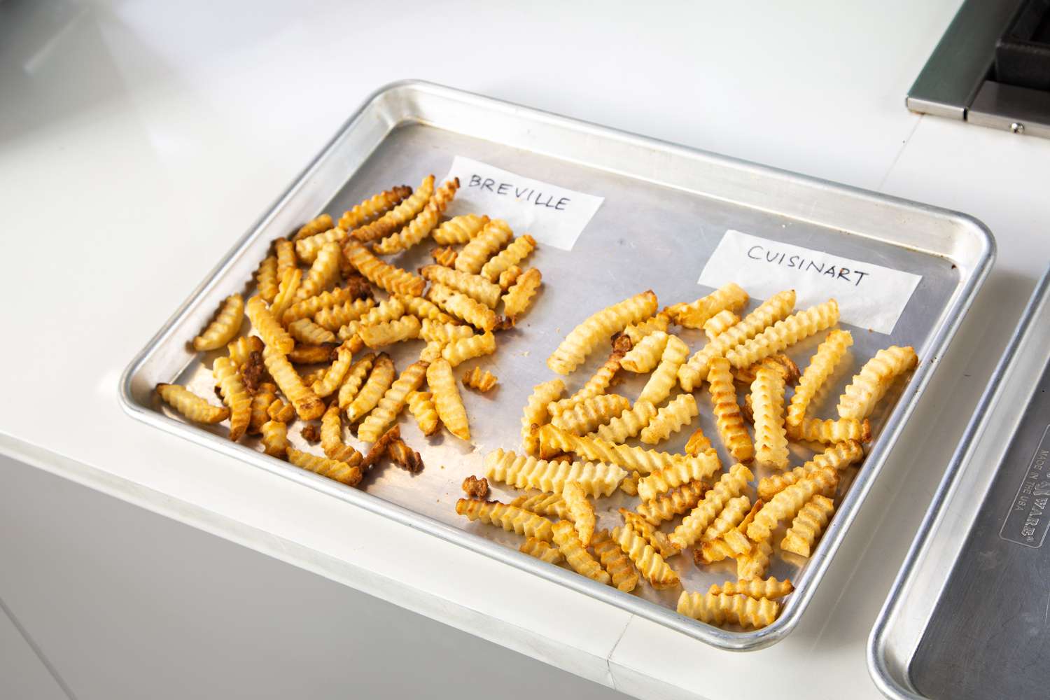 A tray of two piles of French fries with two white cards with the name of an air fryer on each one